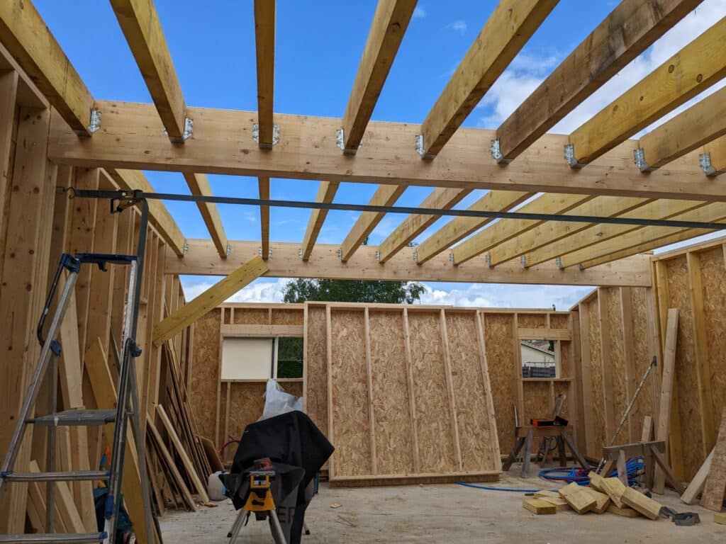 Ossature bois : Pose des solives de toiture et charpente Construction en ossature bois. Solives de toiture fixées par des étriers métalliques. Murs intérieurs en OSB et outils de chantier.