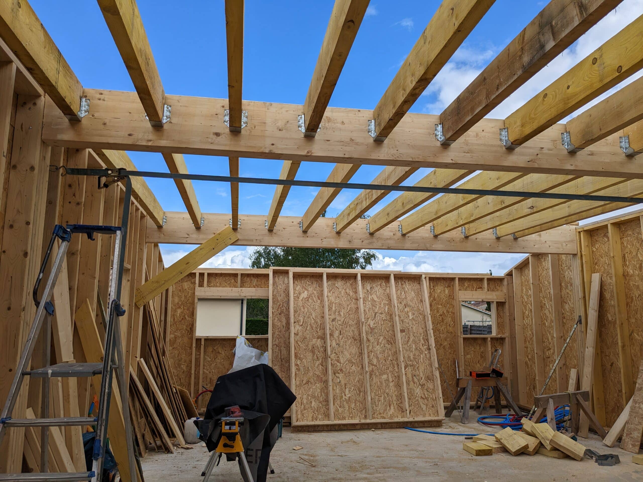Construction en ossature bois. Solives de toiture fixées par des étriers métalliques. Murs intérieurs en OSB et outils de chantier.