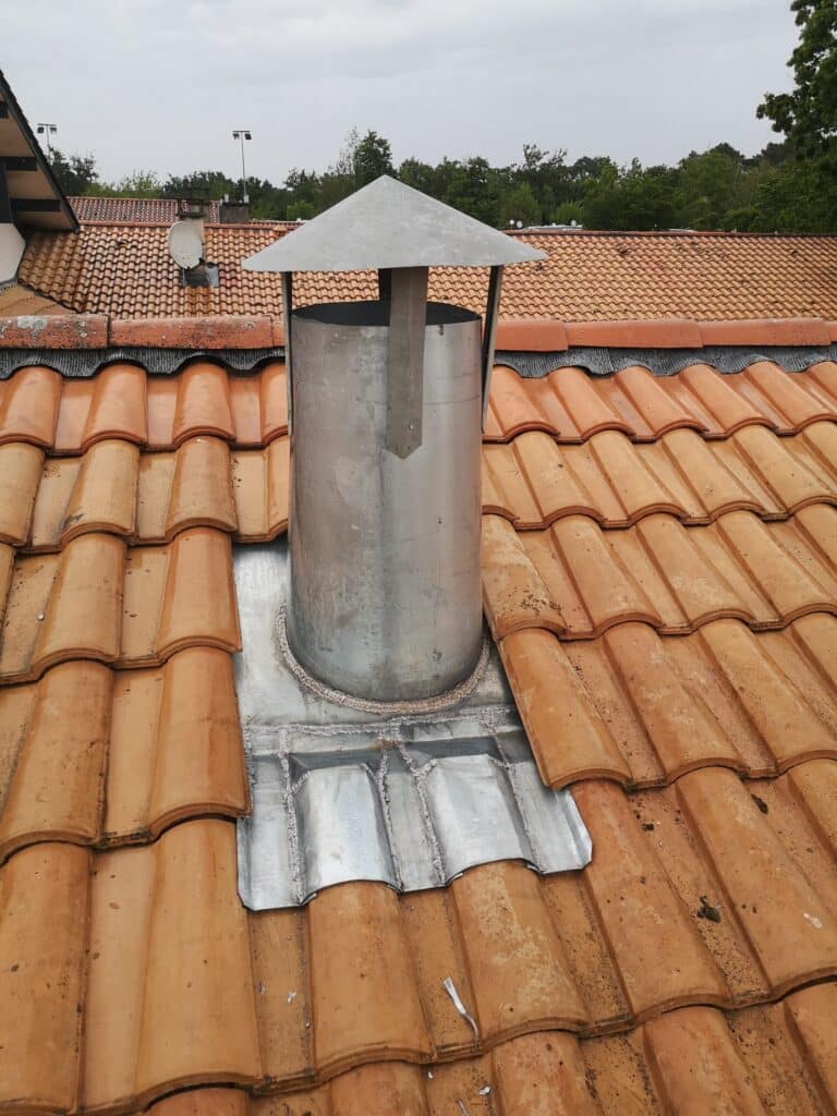 Solin étanchéité cheminée sur toiture tuiles Cheminée métallique cylindrique sur toit en tuiles terracotta. Solin en métal sur mesure avec soudures pour l'étanchéité de la toiture.