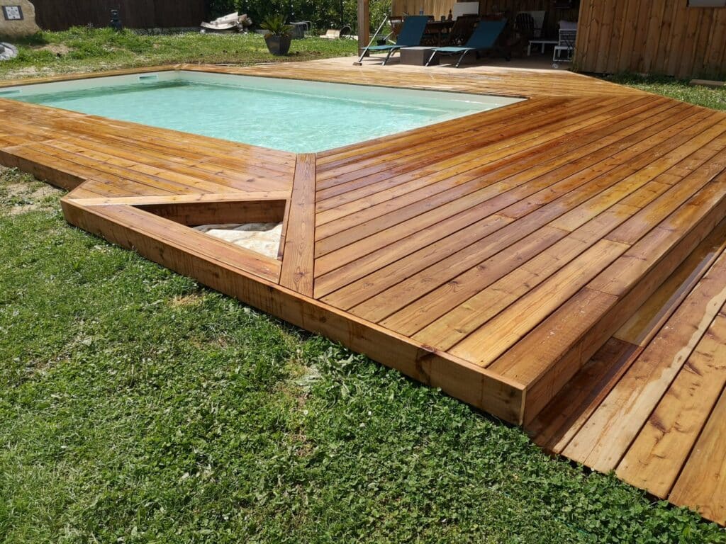 Terrasse de piscine en bois : aménagement extérieur design Terrasse en bois bordant une piscine rectangulaire dans un jardin verdoyant avec chaises longues.